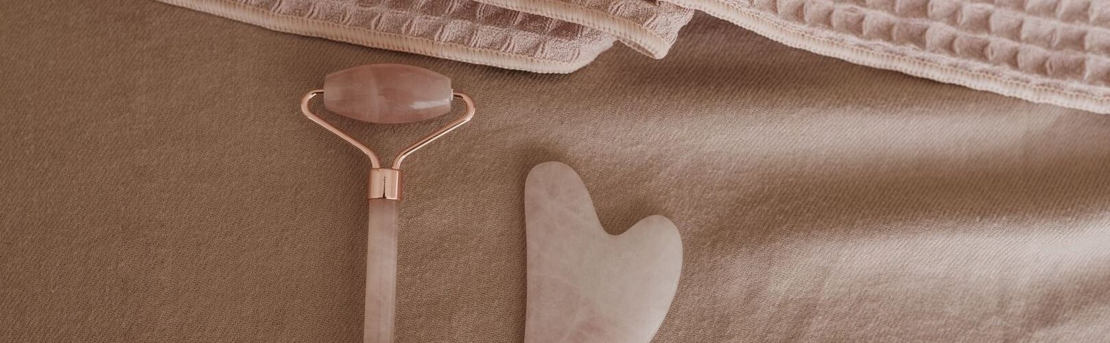 Ruusukvartsinen kasvorulla ja gua sha -kivi neutraalilla tekstiilillä